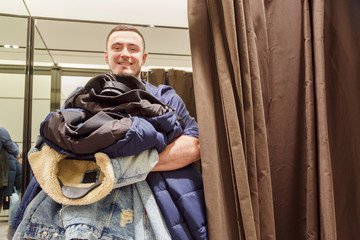 Young man with a armful of clothes in the fitting room during the sale and discounts