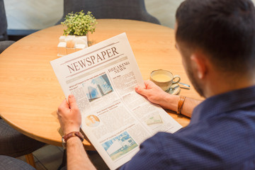 Handsome young man enjoying in cafe reading newspapers and drinking coffee. Back view