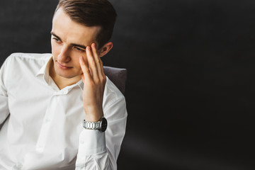 Portrait of a pensive young businessman. Pensive guy in a white shirt sits in a chair