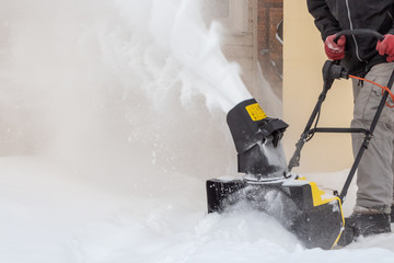 Obraz premium Man is brushing white snow with the yellow electric snow thrower in a winter garden