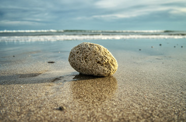 Fototapeta na wymiar Ein runder Stein angespült am Strand in Panama, Fokus auf den Stein, das Meer und die Wellen im Hintergrund