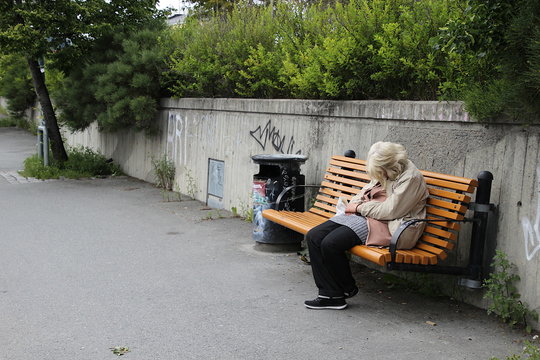 eine alte Frau sitzt allein und verzweifelt auf einer Bank