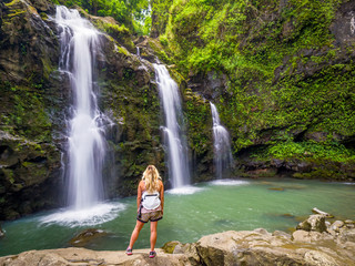 Blonde girl admires Three Bears Falls in Maui, Hawaii Hana Highway - Upper Waikani Falls. Road to...