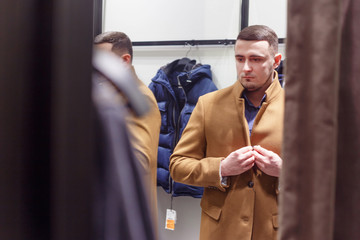 30 years old man trying on an autumn brown classic coat in a fitting room, collection sale.
