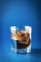 a glass of cold coca soda with ice on a classic blue background, soda bubbles and ice cubes.