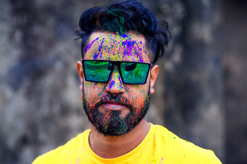Portrait of Indian Man with beard and mustache in powder colors celebrating Holi and looking at...