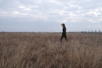 Happy young woman with green jacket and black yoga pants  walking trough high gray grass in autumn. Podgorica , Montenegro