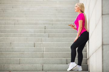 beautiful young woman in sportswear in the summer on the street in headphones with a phone in her hands