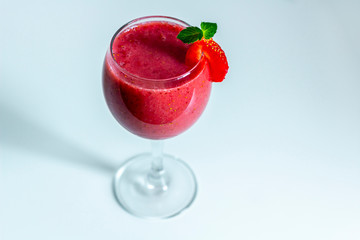 Fresh iced strawberry smoothie in wine glass decorated with slice of strawberries and mint on a light background. Summer Slushy drink. Close up, copy space for text.