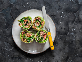 Roasted salmon, avocado puree, green  salad tortilla wrapped roll sandwich on a dark background, top view