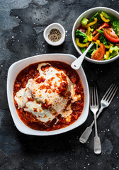Turkey tomato sauce mozzarella cheese meatloaf and fresh tomato yellow bell pepper vegetables salad on a dark background, top view. Healthy balanced diet food