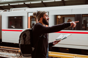 Fototapeta na wymiar .Attractive young man with beard waiting at the train station in Vienna. Thinking about his trip, with the map in his hand and a backpack. Travel photography.