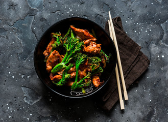 Caramelized stir fry chicken with broccoli on dark background, top view. Asian style food