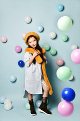 Fototapeta na wymiar Little brunette asian girl in oversized shirt dress, brown beret and scarf, She posing with balloons on blue background.