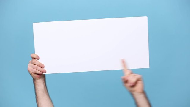 Close up cropped hold in hands blank empty sign white big board for promotional content, pointing finger on place for text isolated on blue background in studio. Copy space advertising area mock up