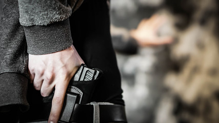 Man holding out hand while drawing a concealed pistol. Personal protection concept - obrazy, fototapety, plakaty