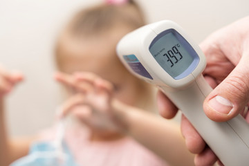 hand with an electronic thermometer is aimed at a small child. on the thermometer the temperature is 39.9