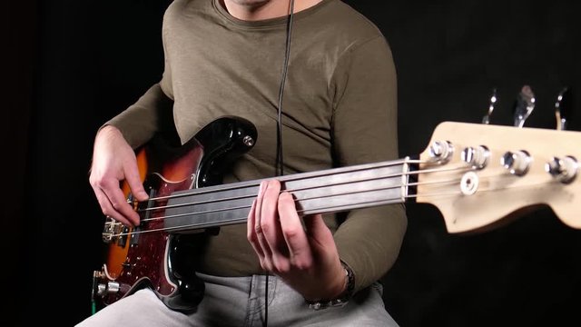 man plays electric bass guitar. Fretless bass. Black background. the color of the guitar is black and red. average plan.
