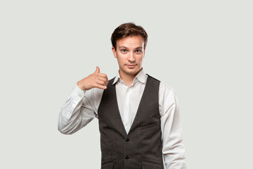 Young businessman in a white shirt and grey vest asking to call him with a hand gesture