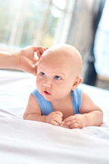 Baby Care. Young mother with little son lying on bed at home touching his head calming down close-up