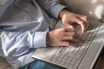 man working on laptop from home, light blue shirt computer keyboard in light gray