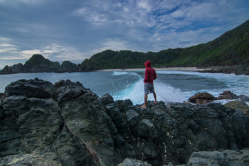 Fototapeta premium Man Standing At Rock Beach With Splash of Wave