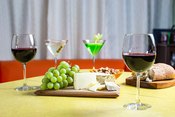 Red wine, martinis, cheese, nuts, grapes and bread on yellow table 