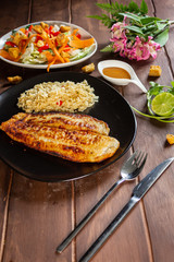 Pescado a la plancha con especias y ensalada de lechuga zanahoria y aderezo mil islas y limon arroz en mesa de madera