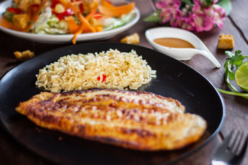 Pescado a la plancha con especias y ensalada de lechuga zanahoria y aderezo mil islas y limon arroz en mesa de madera