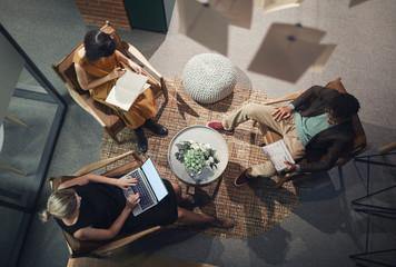 High angle view of young business people sitting on chairs with computer and documents and planning work in team at office