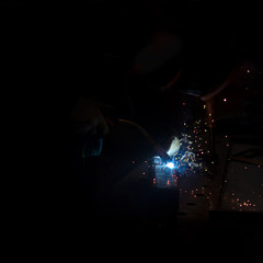 Closeup of MIG welding torch on metal with sparks on completely black background