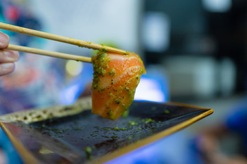 Shot of the man holding chopsticks with salmon sashimi that was covered with seafood dip. selective focus with blurred man in the background.