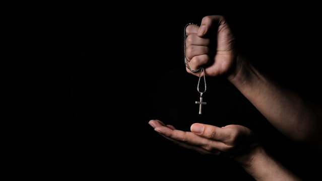 Close-up images of crucifix pendant necklace in man hand on black color background in studio which represent praying for god or jesus and thank gods for giving peaceful and faithful to people