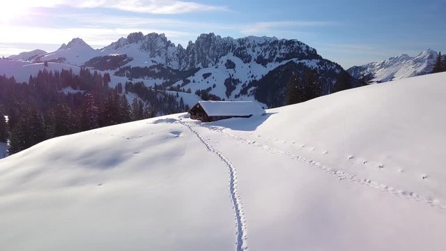 passage by drone on a breathtaking landscape in the sun in the Swiss alps with an uninhabited chalet in the high snow and a typical pointed mountain range in the background