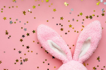 Easter bunny concept. Toy rabbit's ears with stars confetti on pastel pink background. Flat lay, top view, copy space