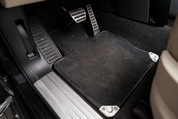 Dirty car floor mats of black carpet with gas pedals and brakes in the workshop for the detailing...