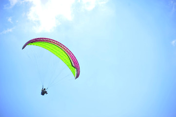 Paraglider flying on colored parachute in blue clear sky at a bright sunny summer day. Active...