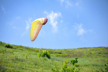 Paraglider flying on colored parachute in blue clear sky at a bright sunny summer day. Active...