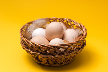 natural ecological eggs and feather in a wicker basket on yellow background with copy space. happy easter
