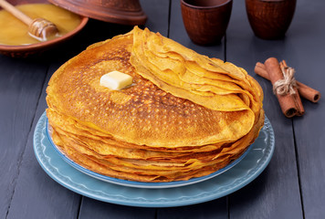 Stack of Pumpkin crepes or russian thin pancakes blini on a plate with honey and butter. The concept of Russian holiday Maslenitsa. Dark wooden background.