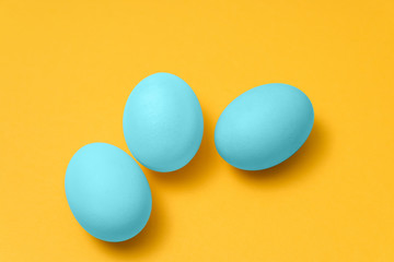 three blue colored eggs on yellow background. easter minimal vivid design