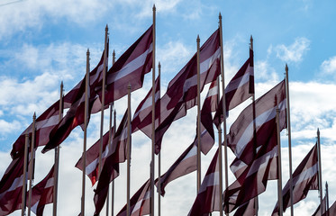 Many Bordeaux white flags of Latvia on a background of cloudy sky