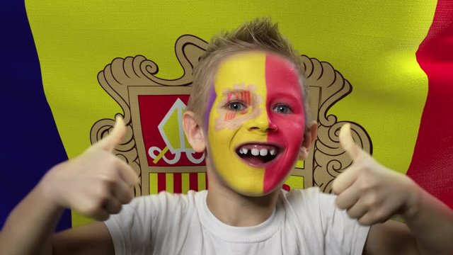 Joyful fan on the background of the flag of Andorra. Happy boy with painted face in national colors. The young fan rejoices in the victory of his beloved team. Success. Victory. Triumph.