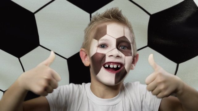 Joyful fan on the background of the flag with a ball print. Happy boy with a painted face. The young fan rejoices in the victory of his beloved team. Success. Victory. Triumph.