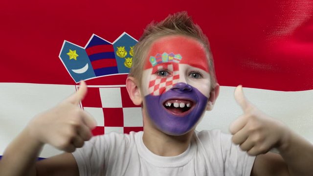 Joyful fan on the background of the flag of Croatia. Happy boy with painted face in national colors. The young fan rejoices in the victory of his beloved team. Success. Victory. Triumph.