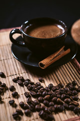 A Cup of coffee and Turkish coffee pot turk among the coffee beans and cinnamon at black background