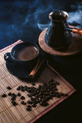 A Cup of coffee and Turkish coffee pot turk among the coffee beans and cinnamon at black background
