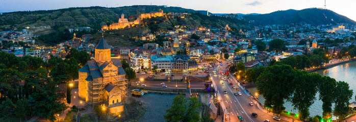 The evening panorama of the old town in the old district of Avlabari, Holy Trinity Cathedral and Rike Park, the Kura river reflects the evening city lights in Tbilisi, Georgia. © miklyxa