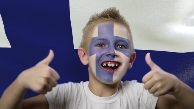 Joyful fan on the background of the flag of Finland. Happy boy with painted face in national colors. The young fan rejoices in the victory of his beloved team. Success. Victory. Triumph.