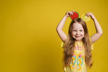 Happy cute little child girl holding slice of fruit over head making ears having fun medium...